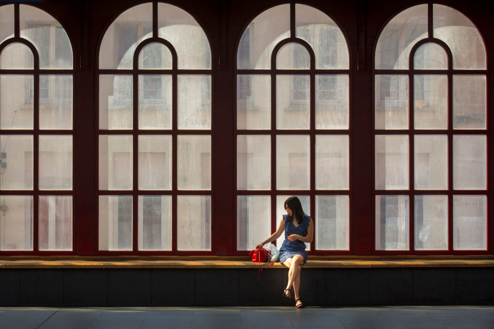 駅の大きな窓辺に、ひとりで座る女性です。