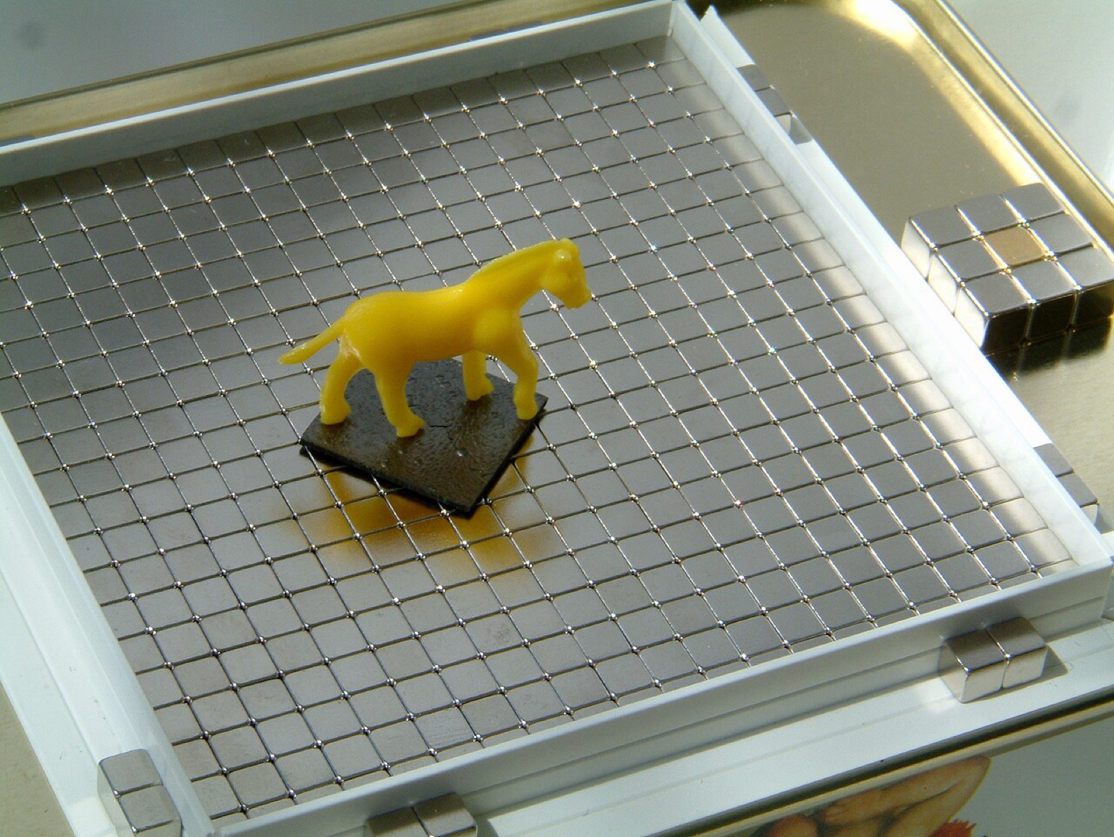 熱分解グラファイトという黒鉛の板が、一辺4mmの立方体の磁石の上に浮き、ゴムの馬を乗せています。磁石は極が市松模様になるように並べてあり、今回の装置の板の下の磁石と同じ並べ方です。