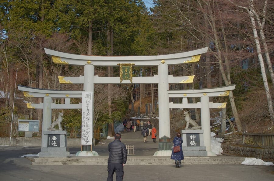 3つの鳥居がつながった形の白い鳥居と、その左右の台座にすわるオオカミの像